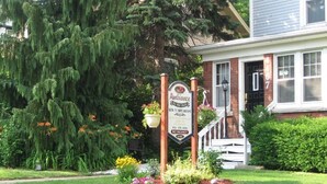 A sign for Ambiance Bed & Breakfast with a front porch and a well-maintained garden. - Ambiance by the Falls B&B (Niagara Falls)