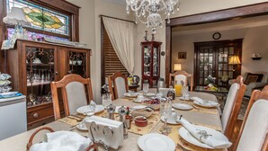 A dining area with a chandelier, wooden furniture, and a stained glass window. - Ambiance by the Falls B&B (Niagara Falls)