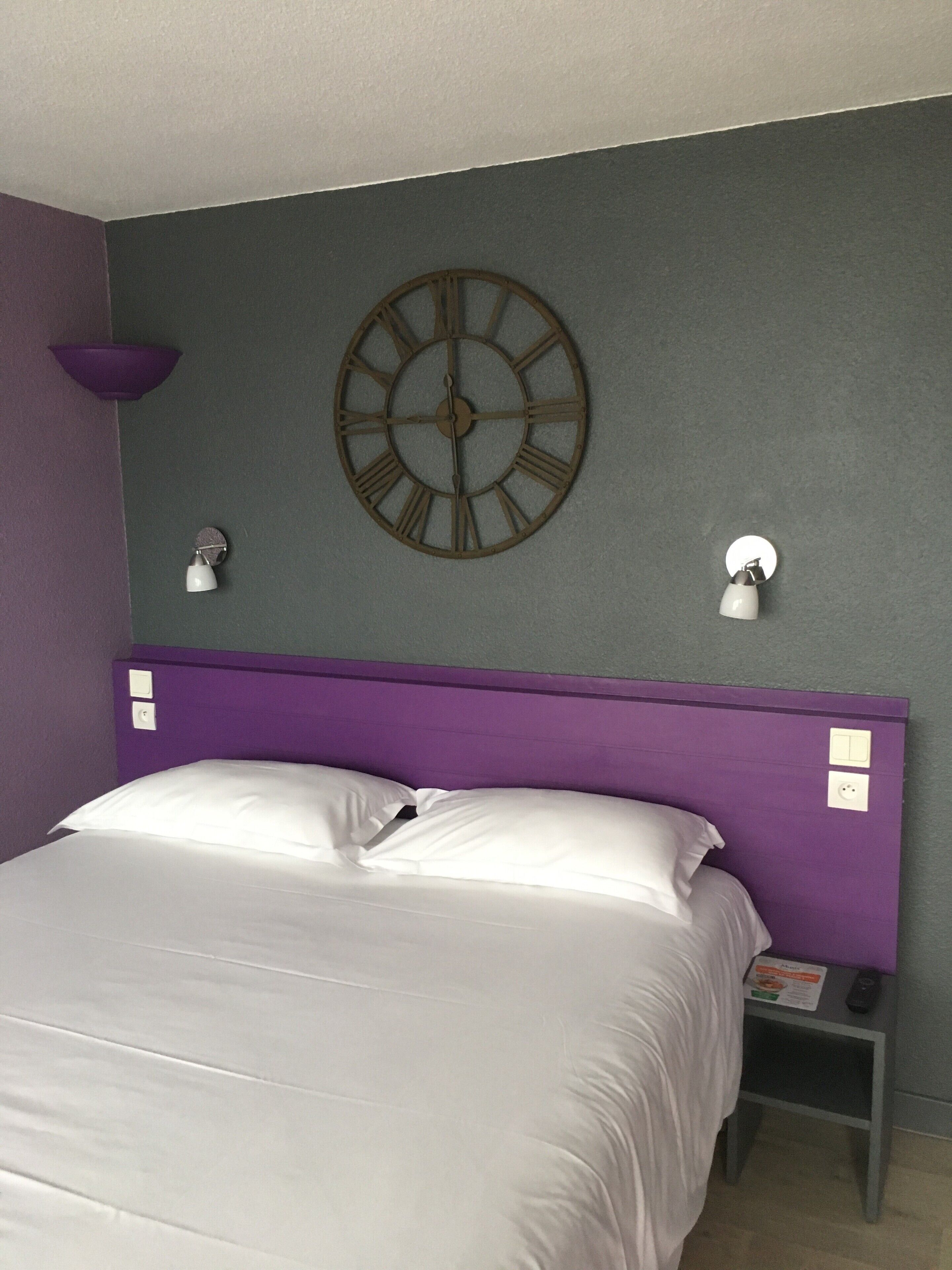 Una habitación con cama, un reloj de pared y dos lámparas de noche.