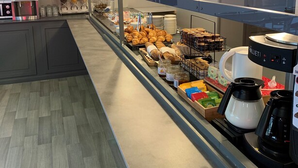 Una vitrina de panadería con pasteles y pan, una máquina de café y una sección refrigerada.