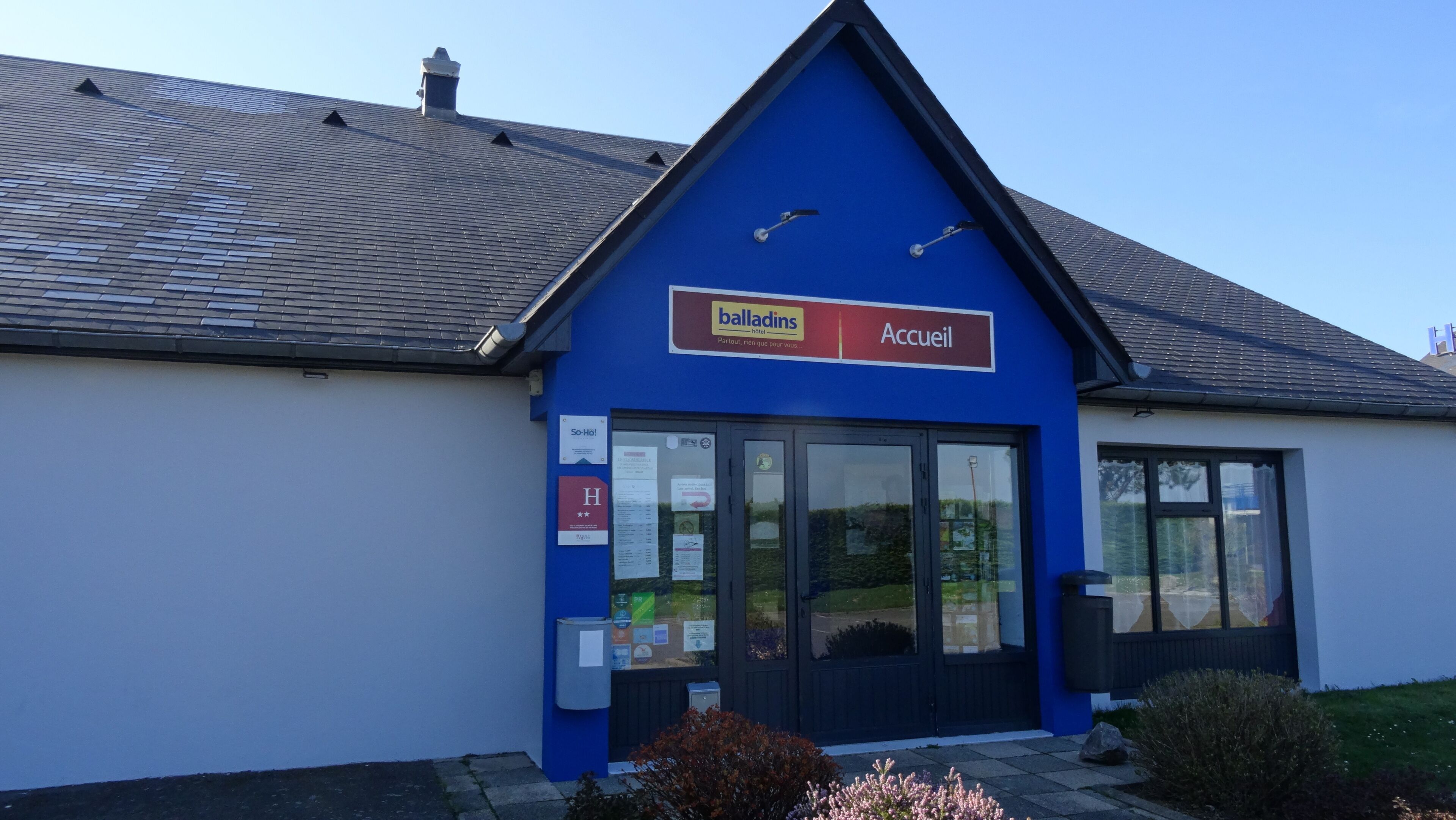 A blue building with a sign reading 'balladins hotel Accueil' and a glass door entrance.