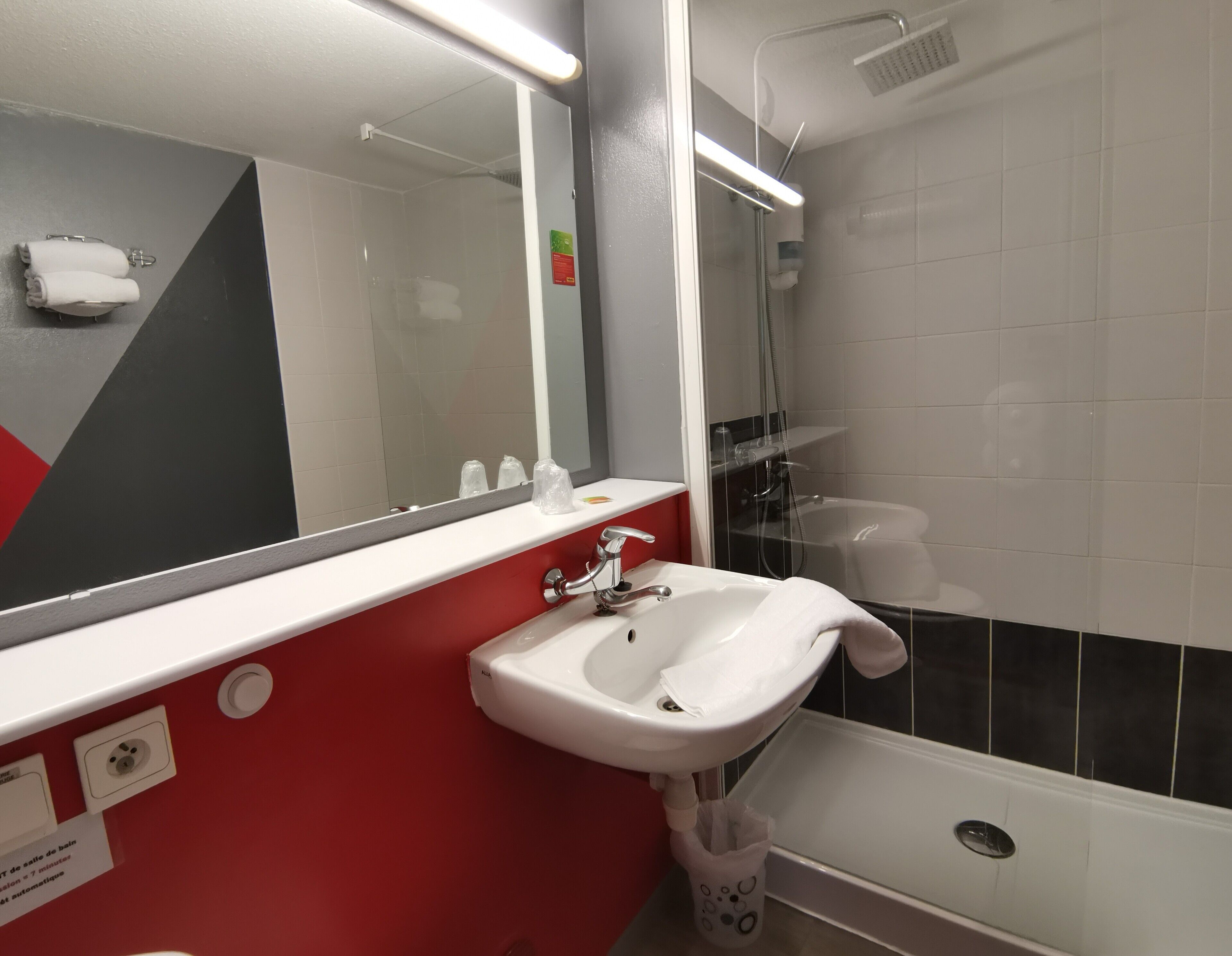 A modern bathroom with a white sink, a mirror, a shower, and a red accent wall.