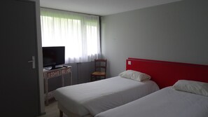 A hotel room with two beds, a television on a wooden desk, a chair, and a window with sheer curtains. - Balladins Dieppe (Saint-Aubin-sur-Scie)