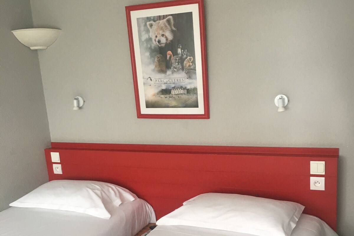 Habitación de hotel con dos camas individuales, cabecera roja, un cartel enmarcado en la pared y una lámpara.