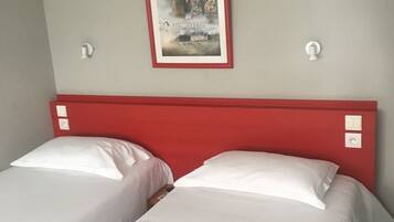 A hotel room with two single beds, a red headboard, a framed poster on the wall, and a light fixture.