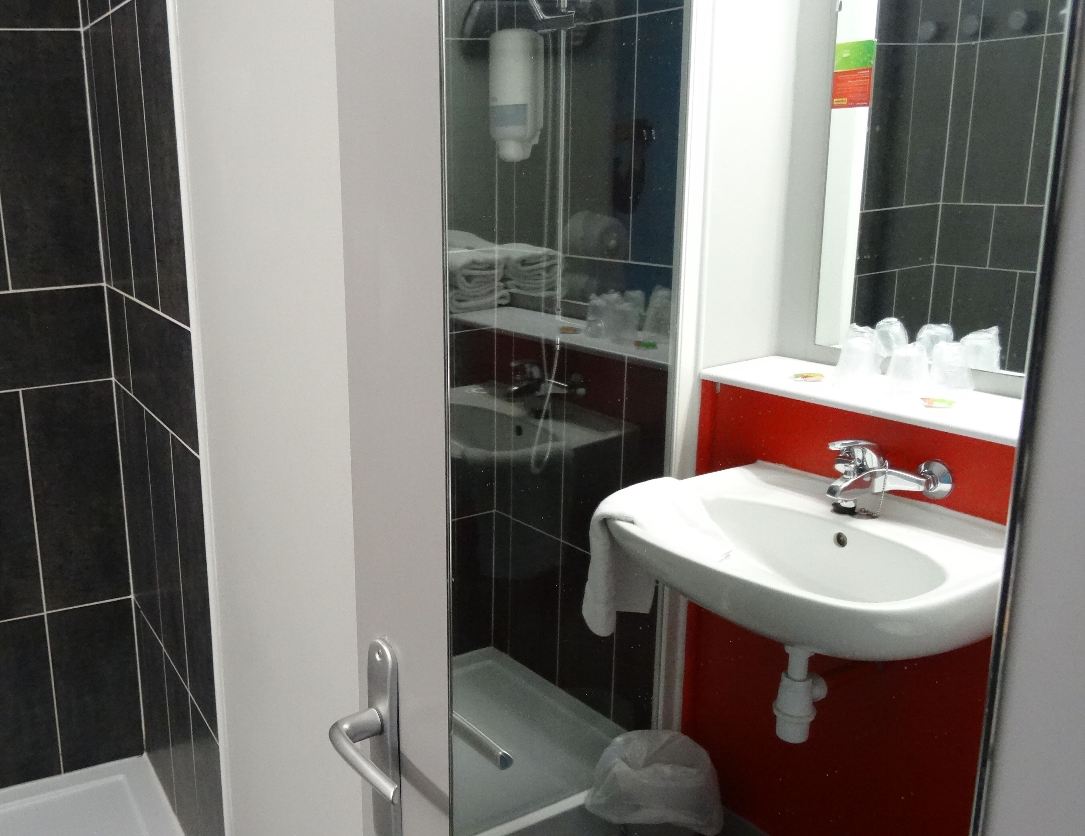 A bathroom with a white sink, red cabinet, and a glass shower enclosure.