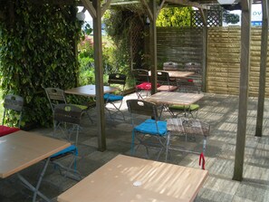 An outdoor patio with tables and chairs, surrounded by greenery and a wooden fence. - Balladins Dieppe (Saint-Aubin-sur-Scie)