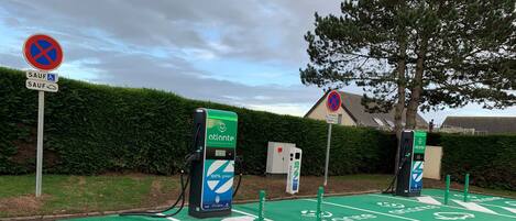 A green parking area with electric vehicle charging stations and a sign indicating '3 places SAUF'.