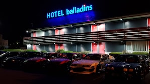 Un hotel con un letrero de neón, varios espacios de estacionamiento y una fachada de edificio moderna.