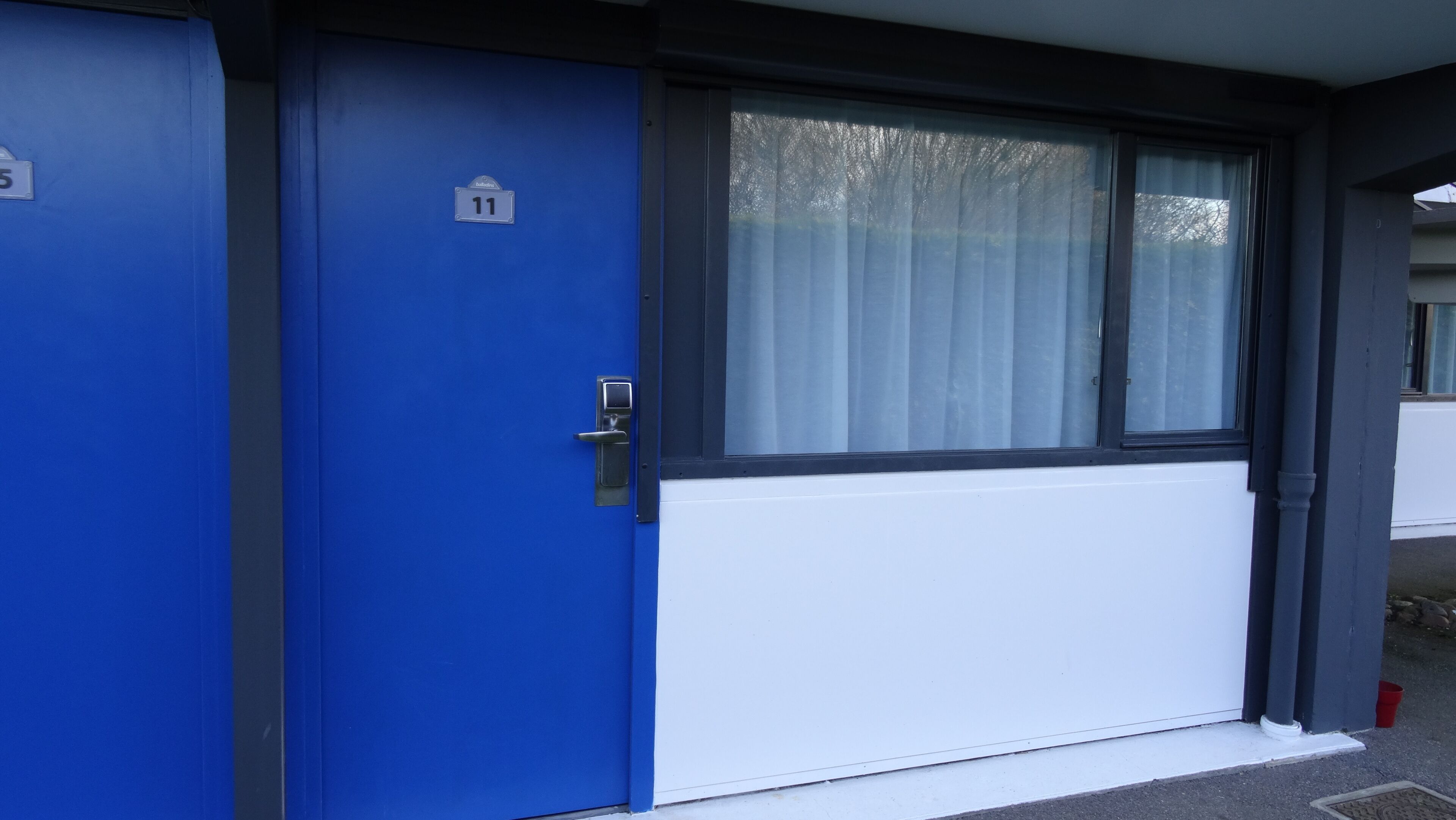 A blue door with a number 11 sign, a window with a white blind, and a white wall.