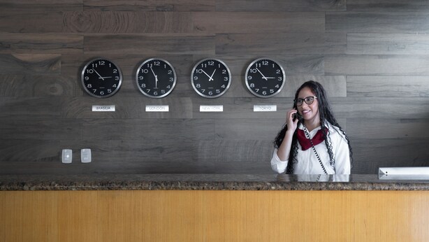 A reception desk with four clocks displaying times from different cities. - Carlton Express - Antigo Plaza Hotel (São José dos Campos)