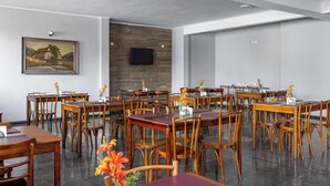 A dining area with multiple wooden tables and chairs, a flat-screen TV mounted on the wall, and a painting on the left wall. - Carlton Express - Antigo Plaza Hotel (São José dos Campos)