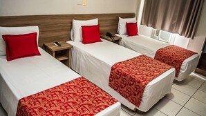 A hotel room with three single beds, each with a white mattress and red bedding. There are bedside tables with a remote control and a phone on one. - Carlton Express - Antigo Plaza Hotel (São José dos Campos)