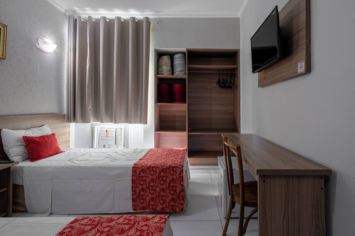 Una habitació d'hotel amb un llit, un escriptori, una cadira, un televisor penjat a la paret i un armari amb prestatges.