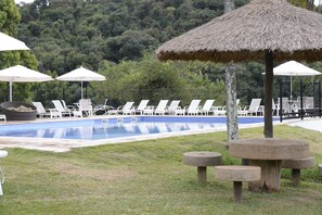 A pool area with lounge chairs and umbrellas, surrounded by a fence and trees. - Hotel Fazenda Capoava (Itu)