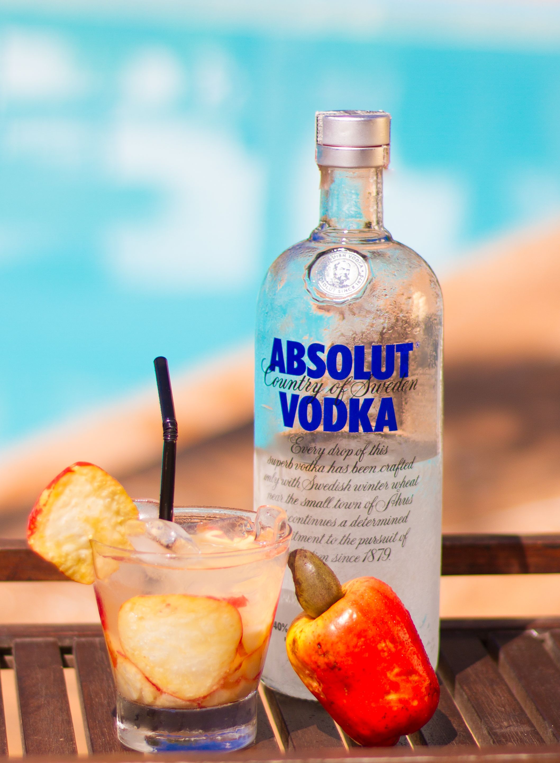 Une bouteille de vodka Absolut et un verre contenant une tranche de pomme et une paille.