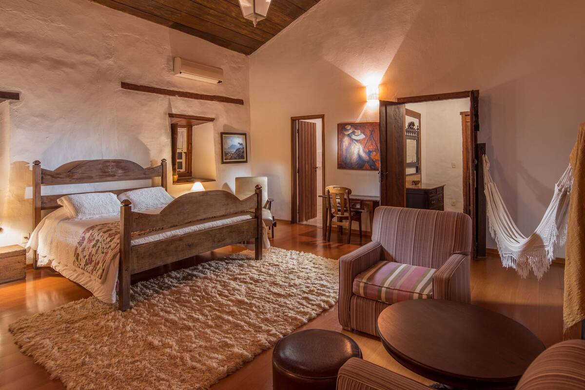A cozy bedroom with a wooden bed, a small table, a chair, and a hammock.