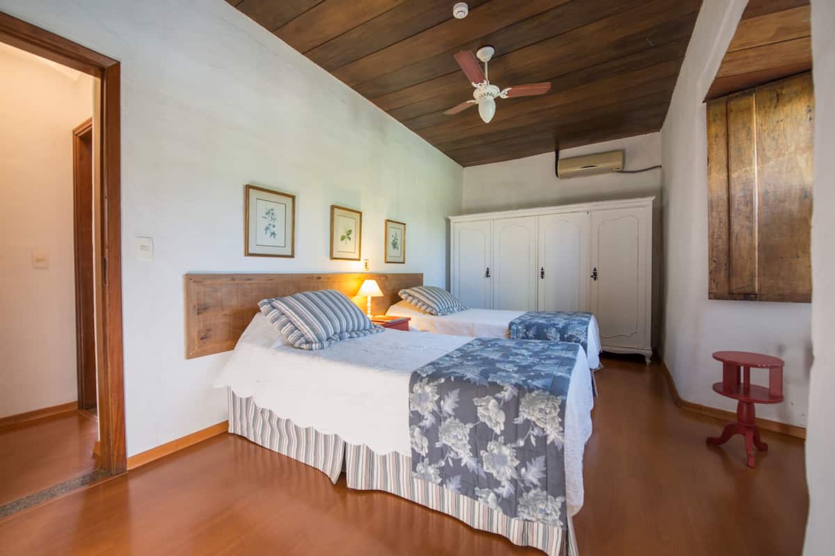 A bedroom with two beds, wooden flooring, a ceiling fan, and a wardrobe.