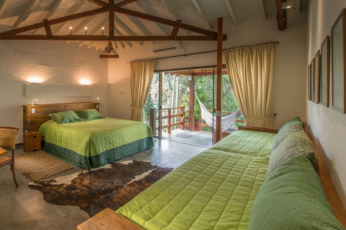 A bedroom with a wooden desk, two beds, a large rug, and a view of the outdoors.