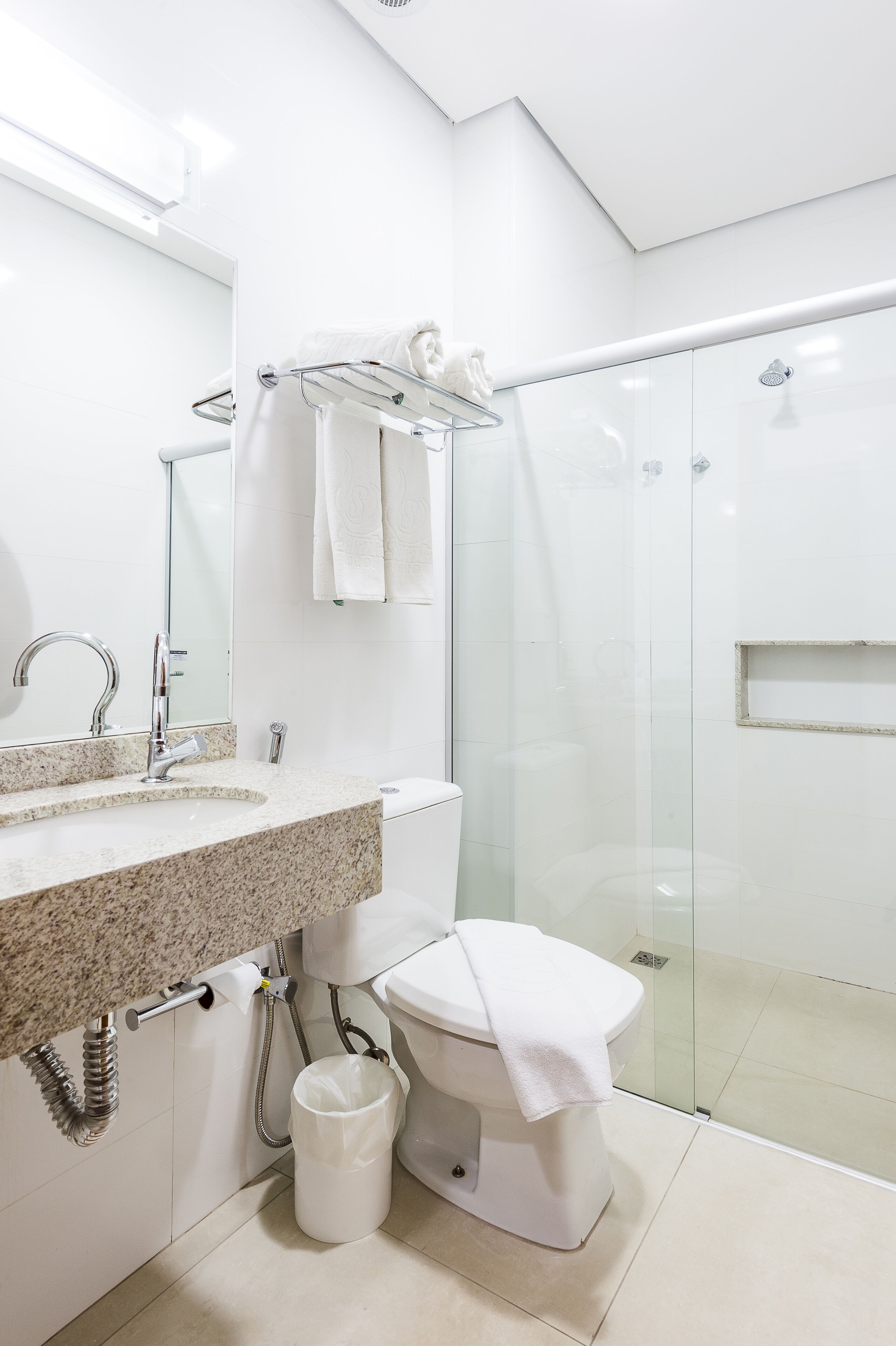 A modern bathroom with a granite countertop, a toilet, a glass shower enclosure, and a towel rack.