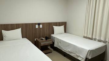 Habitación de hotel con dos camas, una mesita de noche con teléfono y control remoto, y una ventana con cortinas.