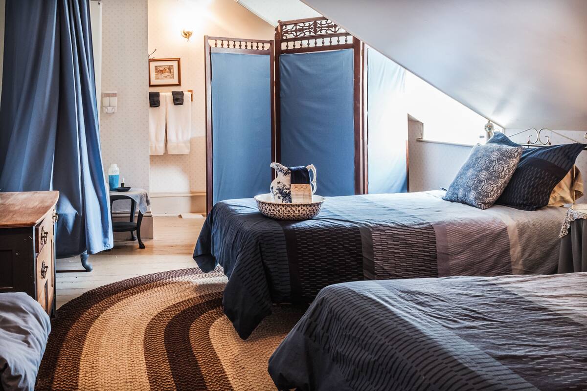 A bedroom with two beds, a wooden dresser, a blue curtain, and a decorative wall panel.