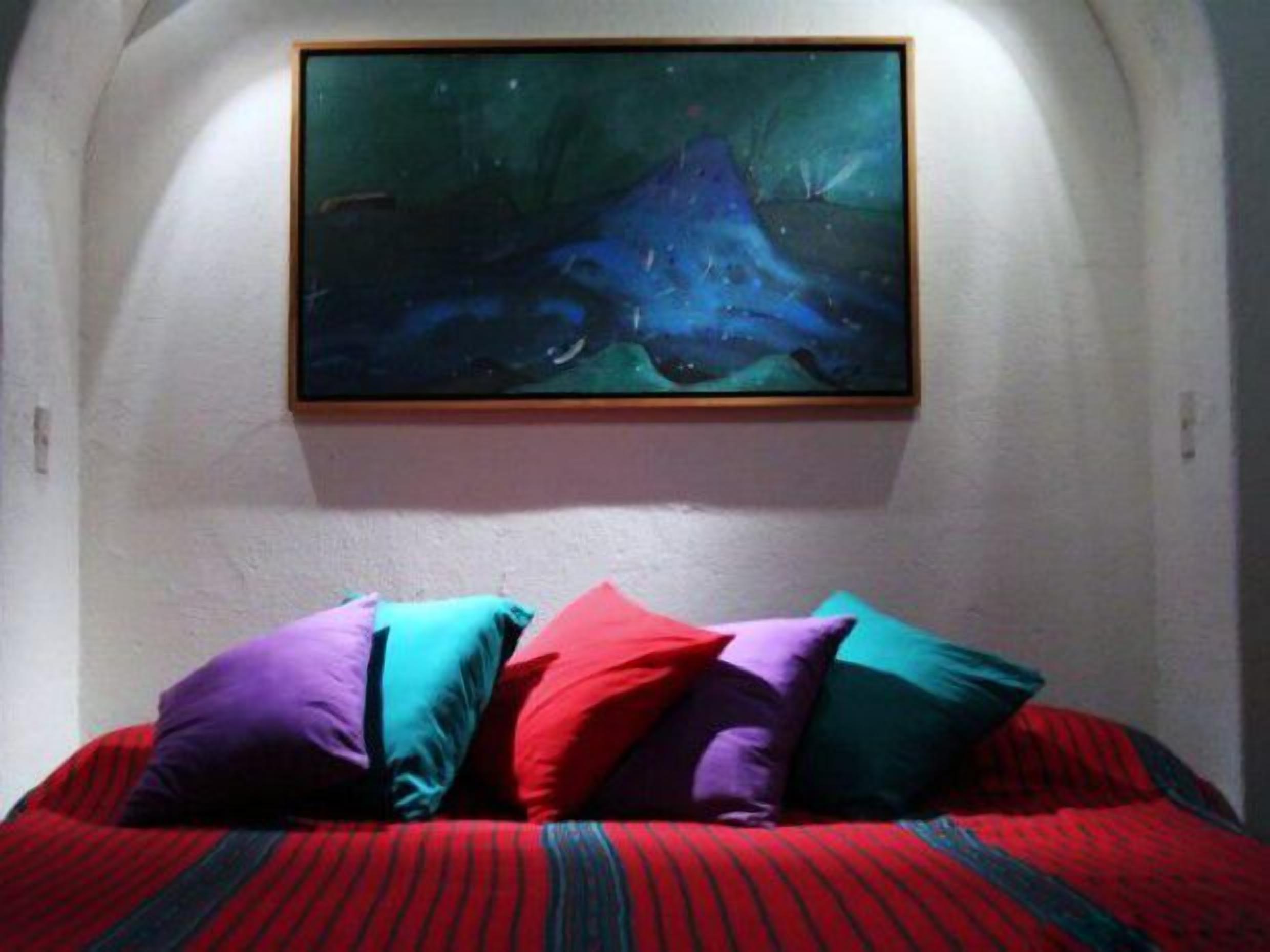 Une chambre à coucher avec un lit, des coussins colorés et un tableau au mur.