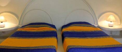 Two beds with striped bedding in a room with a curved ceiling and bedside lamps.