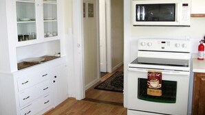 A kitchen with white cabinets, a microwave, and an oven. - Sea Whale Cottages (Middletown)