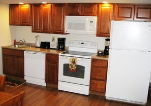 A kitchen with wooden cabinets, a white microwave, a stove, and a refrigerator. - Sea Whale Cottages (Middletown)