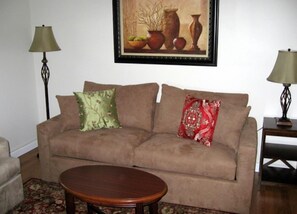A living room with a beige sofa, two lamps, a framed painting, and a wooden coffee table. - Sea Whale Cottages (Middletown)
