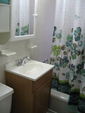 A bathroom with a white sink, wooden cabinet, and a shower curtain with a floral pattern. - Sea Whale Cottages (Middletown)