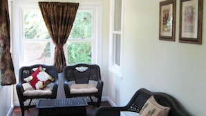 A cozy room with wicker furniture, including two chairs and a sofa, a small table, and a window with curtains. - Sea Whale Cottages (Middletown)