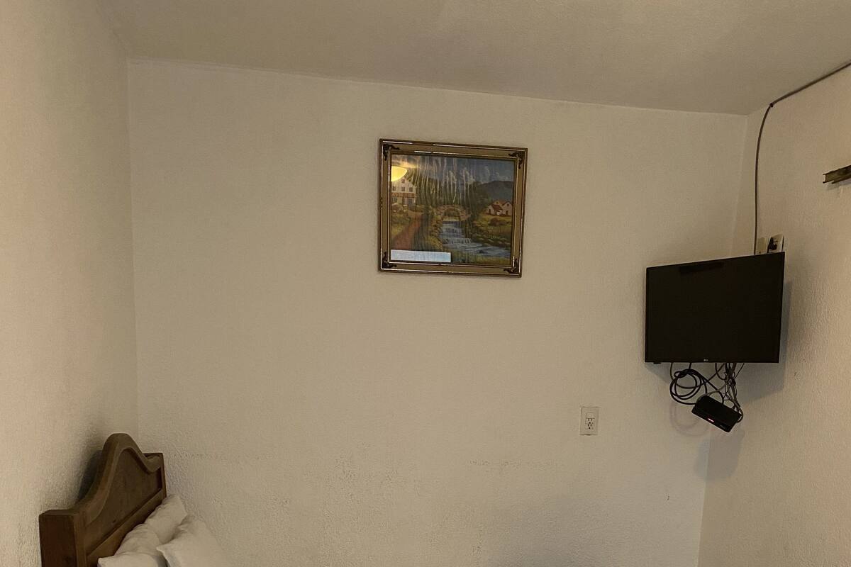 A room with two beds, a painting on the wall, and a TV mounted on the wall.