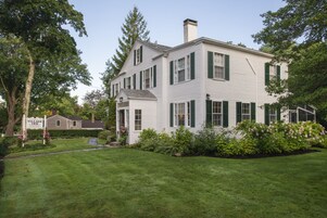 A two-story white building with green shutters, a sign indicating it is a Village Inn, and a well-maintained lawn.