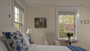Une chambre avec un grand lit, une chaise, une petite table avec une lampe et une fenêtre donnant sur des arbres.