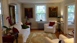 Un salon bien éclairé, avec des meubles blancs, une grande fenêtre et un radiateur.