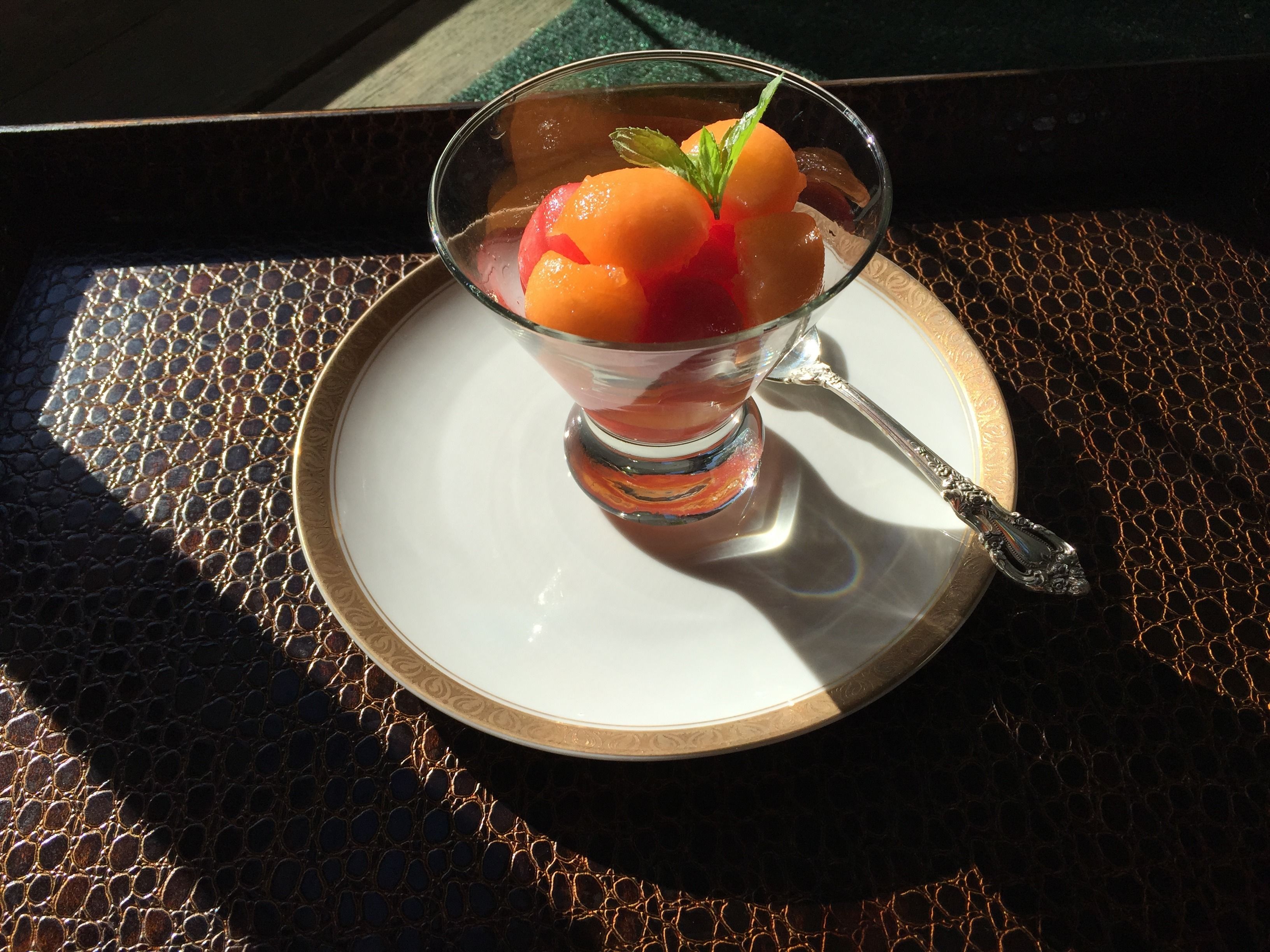 Postre en un vaso sobre un platillo, con una cuchara, colocado sobre una mesa con textura.