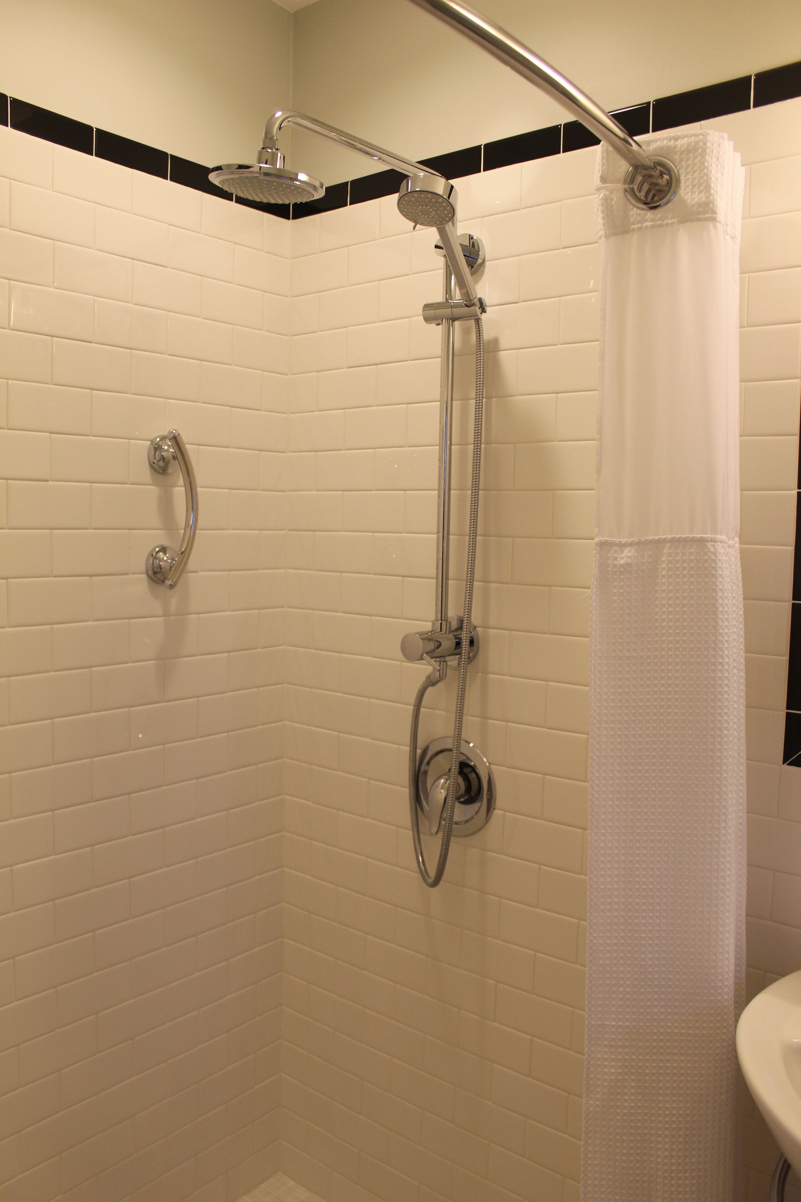 A shower with a handheld showerhead, a handheld showerhead, and a shower curtain.