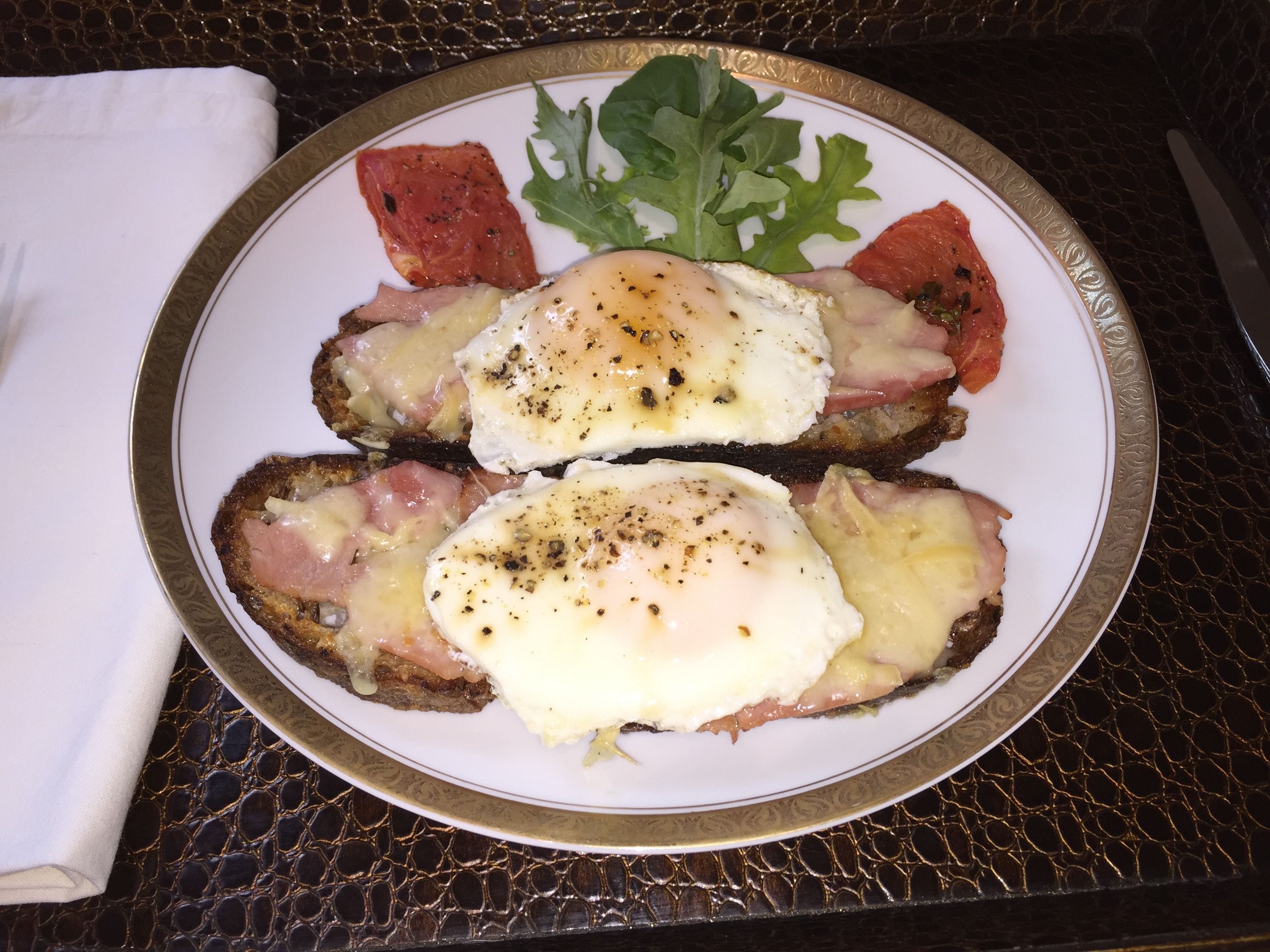 A plate with two poached eggs on toast, accompanied by a leaf of arugula and a slice of tomato.