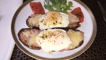 A plate with two poached eggs on toast, accompanied by a leaf of arugula and a slice of tomato.