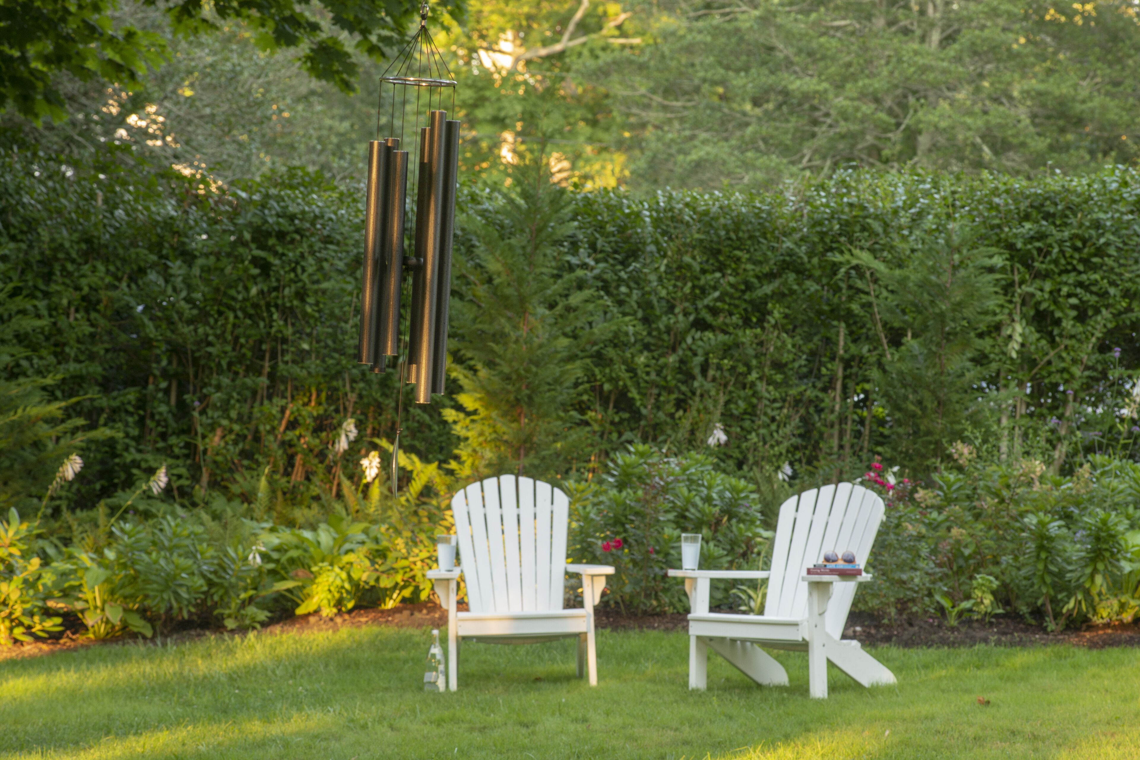 Deux chaises Adirondack blanches se trouvent dans un jardin luxuriant, avec un feuillage dense en arrière-plan.