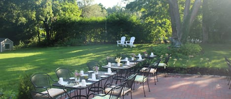 Une terrasse extérieure avec des tables et des chaises, entourée d’une pelouse bien entretenue et d’arbres.