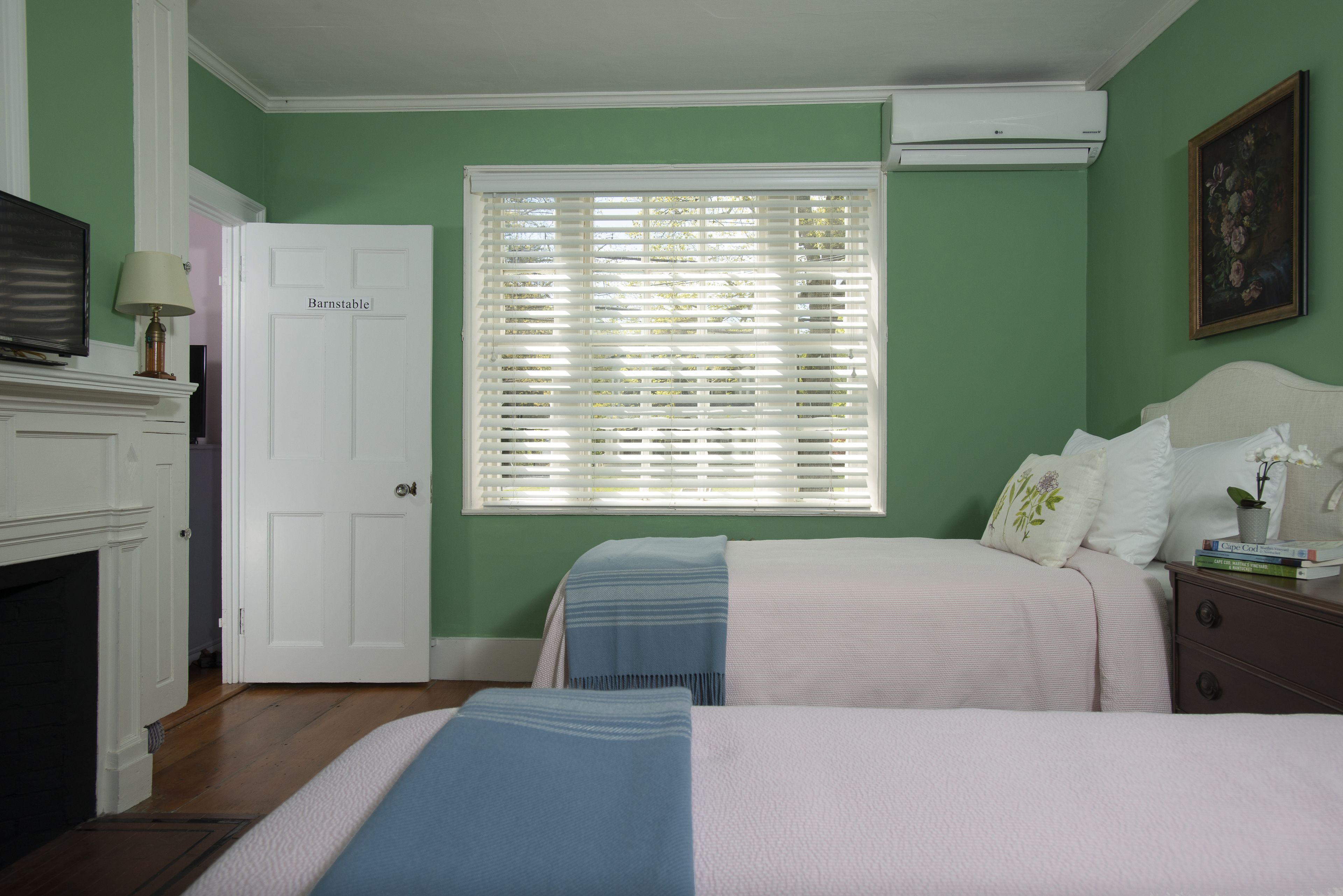 A bedroom with two beds, a white door, a fireplace, and a window with blinds.