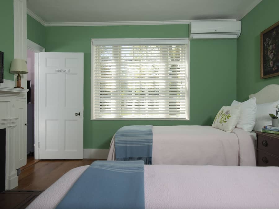 A bedroom with two beds, a white door, a fireplace, and a window with blinds.