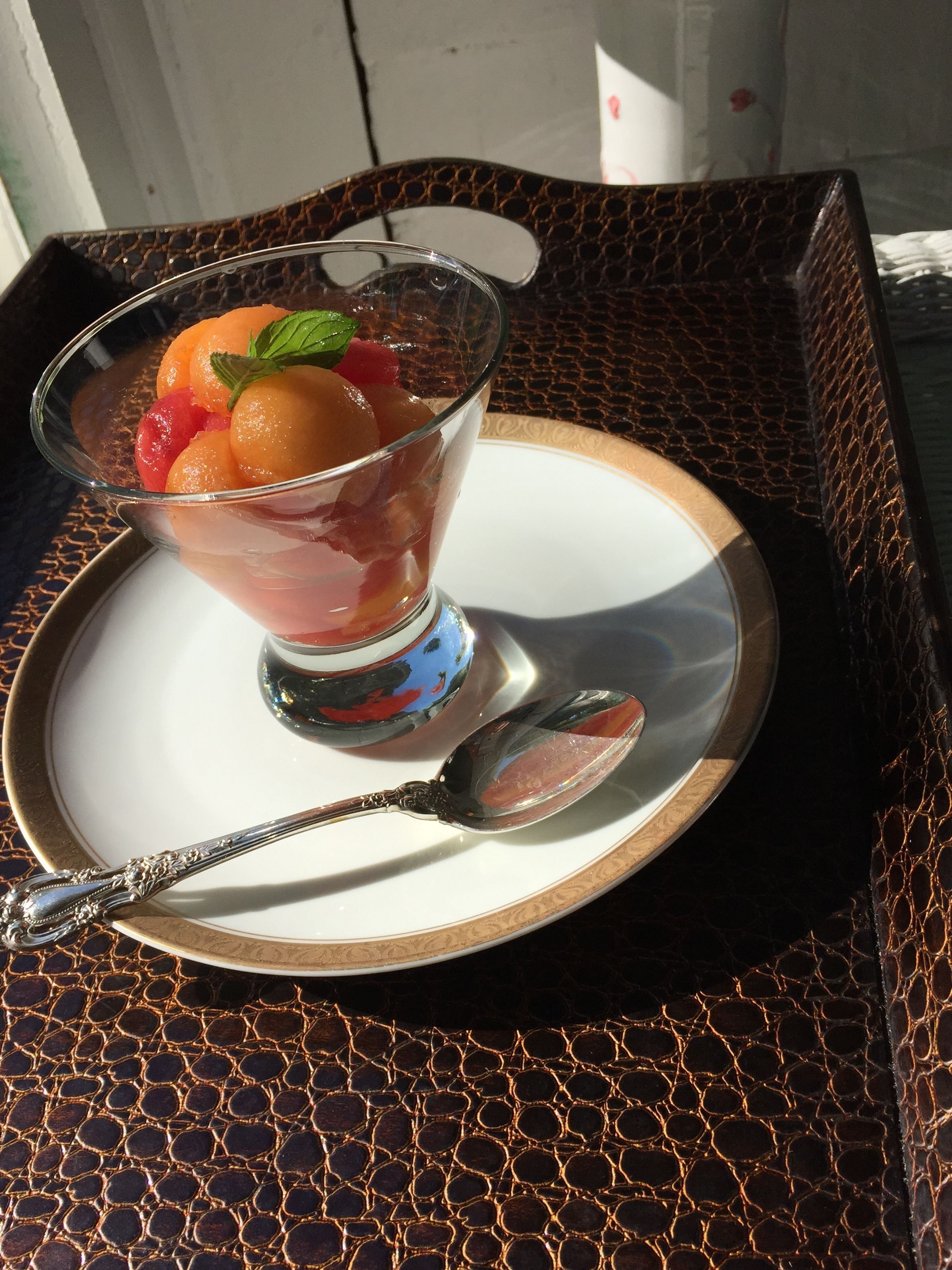 A dessert in a glass bowl on a white plate with a spoon, placed on a textured table.