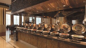 A buffet area with multiple serving stations, a stone accent wall, and modern lighting fixtures. - Wyndham Urumqi North (Miquan)