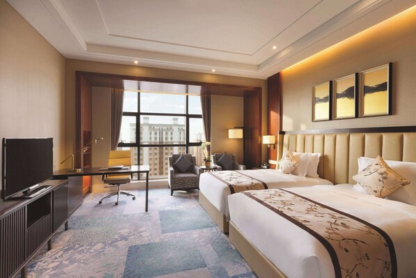 A hotel room with two beds, a desk, a television, and a large window with a city view.