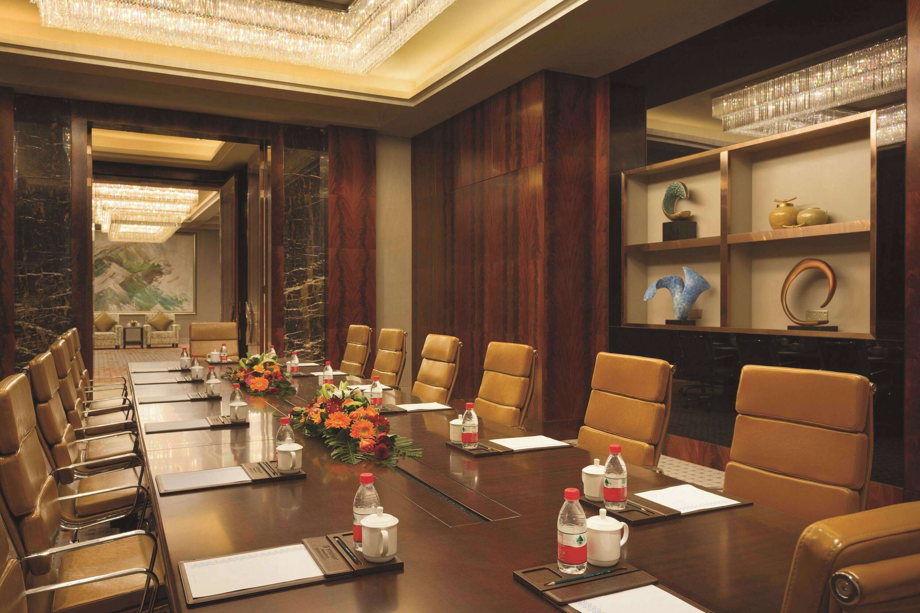 A conference room with a long table, leather chairs, water bottles, and a floral centerpiece.