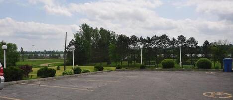 A parking lot with a clear sky, trees, and a distant golf course.